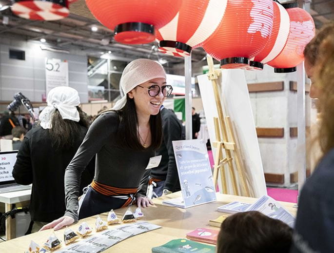 Femme exposante souriant derrière son stand